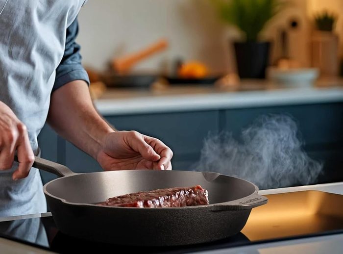 Gusseiserne Pfanne auf dem Herd, darin brät ein Stück Fleisch